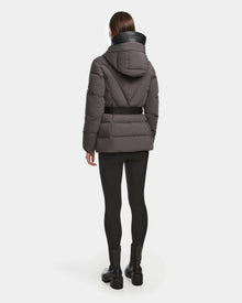 A person stands facing away, wearing the Rudsak ENZAH - 8124692 grey RDS-certified down jacket with a black belt, large hood, and high collar. The outfit includes black leggings and ankle boots, set against a plain white background.