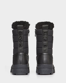 The REAGAN - 6222500 BLACK men’s winter boots by Rudsak feature black leather, thick soles, quilted uppers, and black faux fur lining. Rudsak branding appears on the heel, pull tab, and side. Shown from the back.