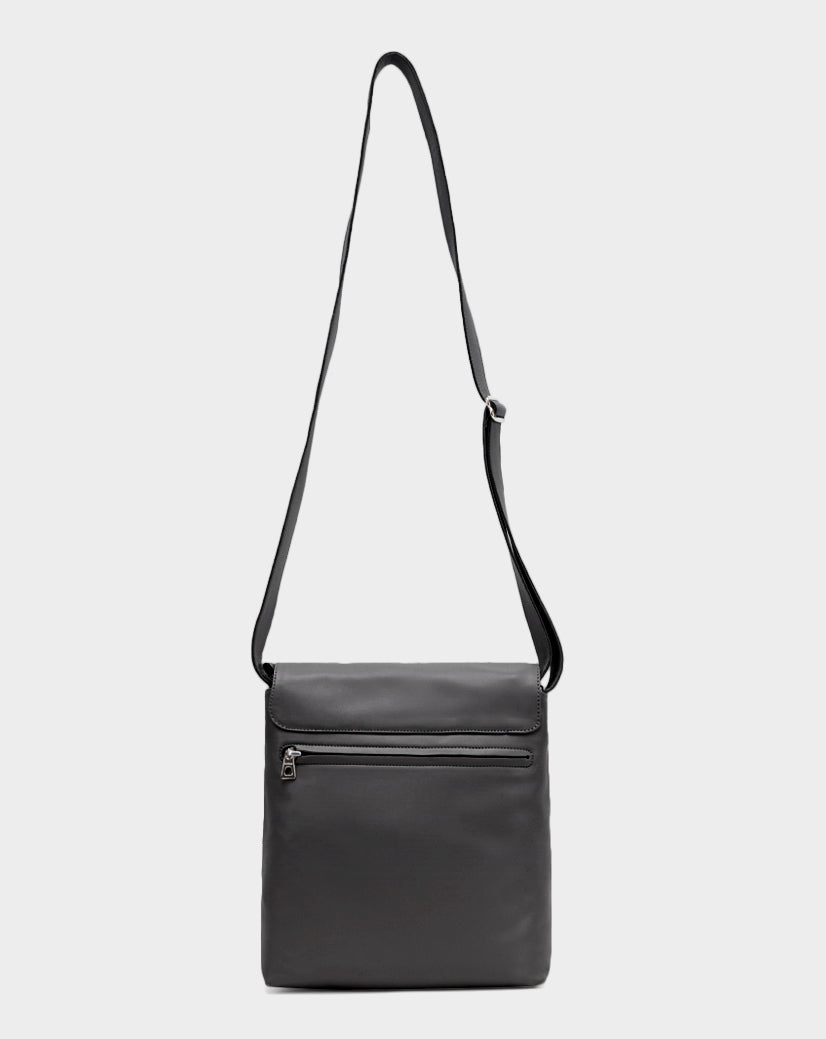 The Rudsak MADDY - 8322512 BLACK is a minimalist black leather messenger bag with an adjustable strap, front zippered pocket, and rectangular shape, shown against a plain light gray background.