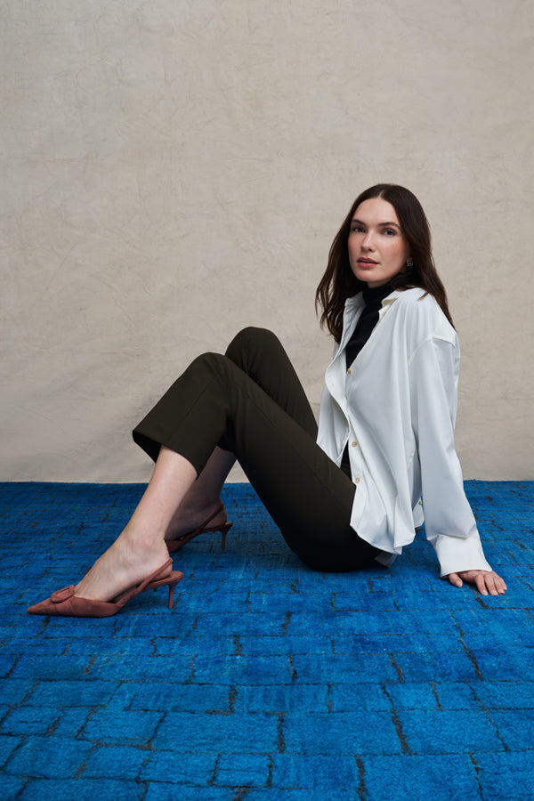 Woman wearing a white long sleeve button down and skinny black pants on a blue carpet floor and against a beige background | Exclude