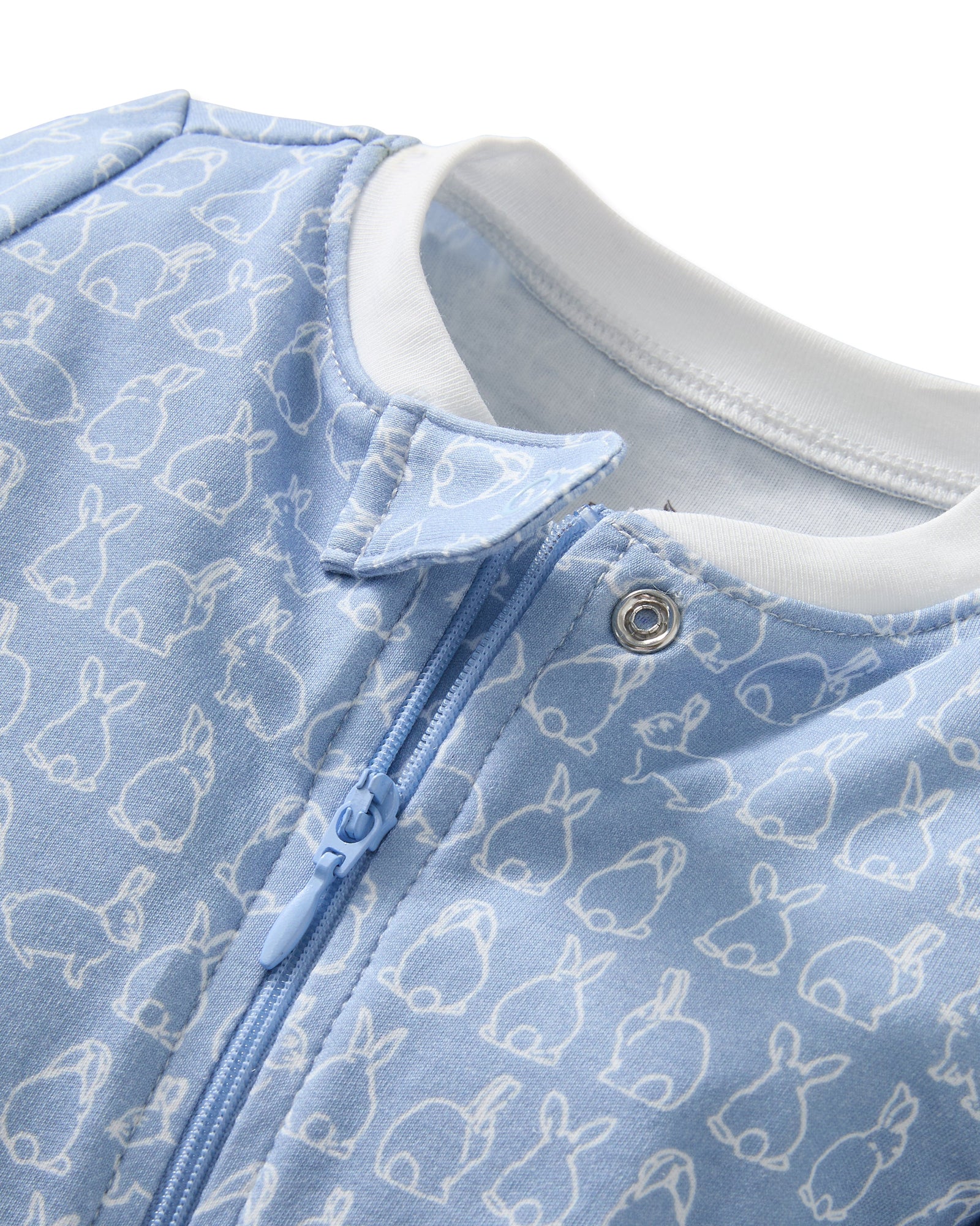 The Baby's Pima Romper in Hoppy Days Blue features a blue footed design with white cuffs, a white collar, white-outlined bunny pattern, and a diagonal zipper from neck to leg.