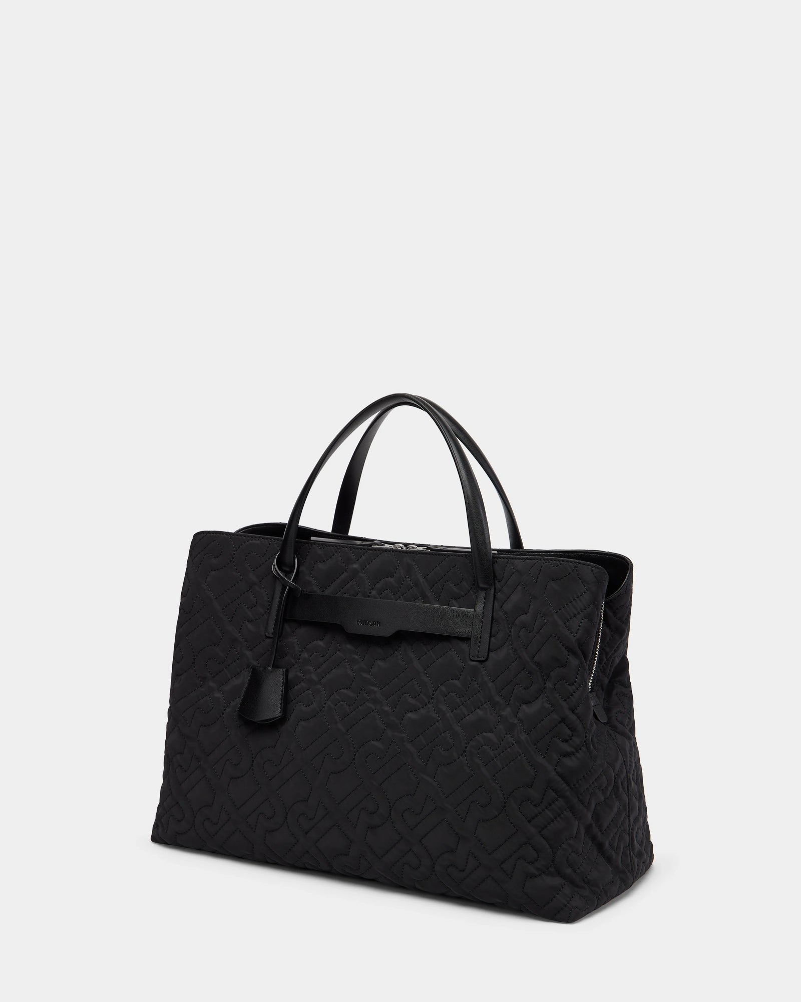 The ASMINE - L325005 Black by Rudsak is a large black bag with dual handles, an embossed pattern, and a small hanging tag, shown against a plain light gray background.