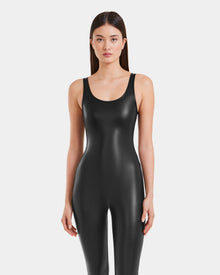A woman with straight brown hair stands facing forward, wearing the LAWREN - 8523047 Black sleeveless vegan leather bodysuit by Rudsak against a plain white background.
