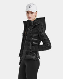 Wearing the Excluded MELISSA - 8121000 BLACK fitted puffer jacket, black leggings, and a white baseball cap with an R logo, a person stands against a plain light background.