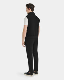 A man stands facing away, wearing the Rudsak MERLO - 6124017 Black quilted vest over a white short-sleeve shirt, black pants, and black shoes with white soles against a plain white background.