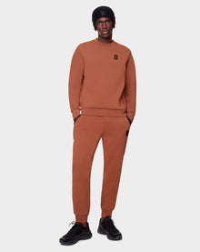 A man faces forward against a plain background wearing the Rudsak DEVAN - 9522510 COHIBA MEN lounge sweater and joggers, paired with black sneakers and a black beanie, hands in his pockets.