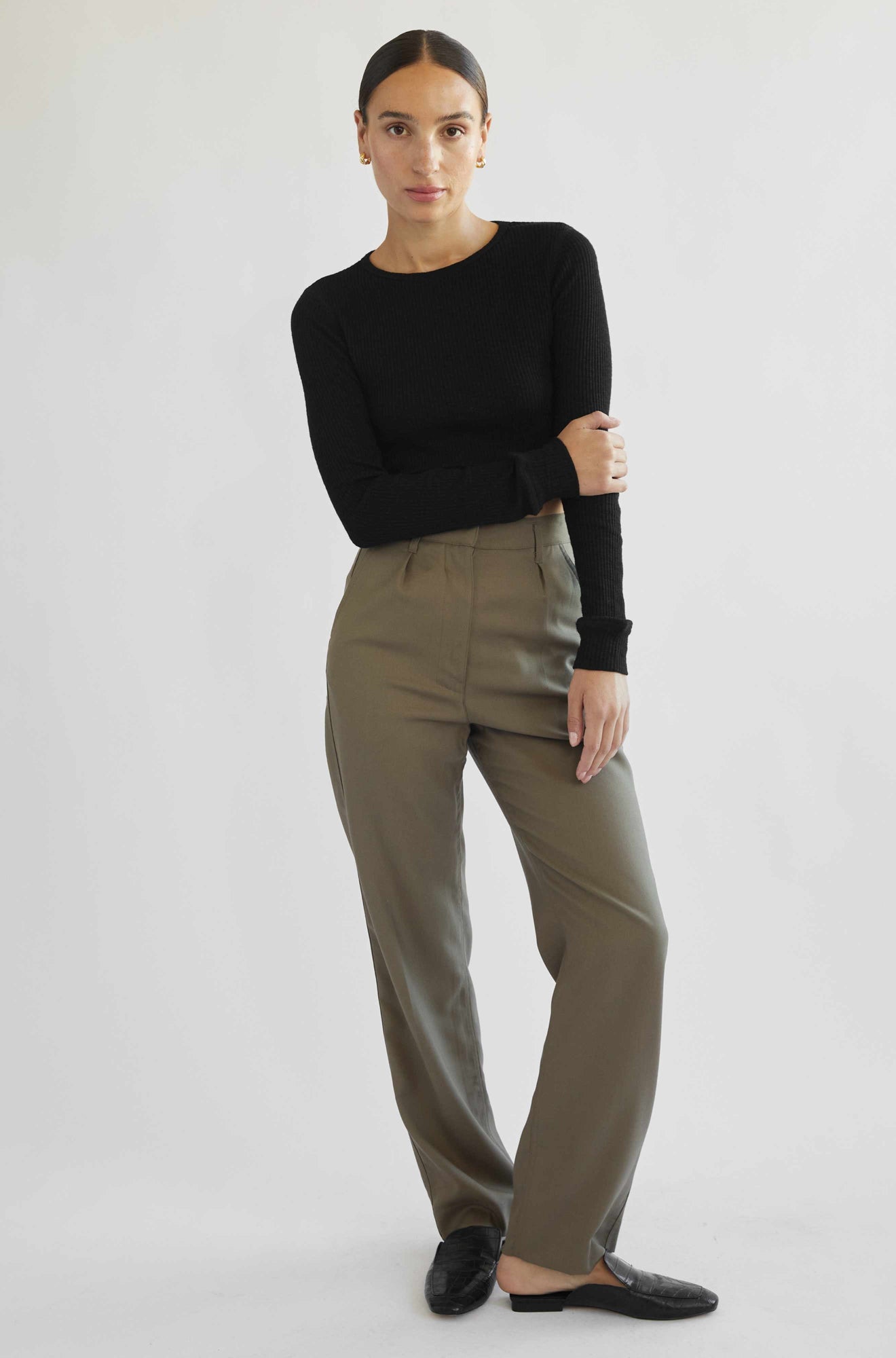 Woman wearing a black long-sleeve top and beige pants on a white background