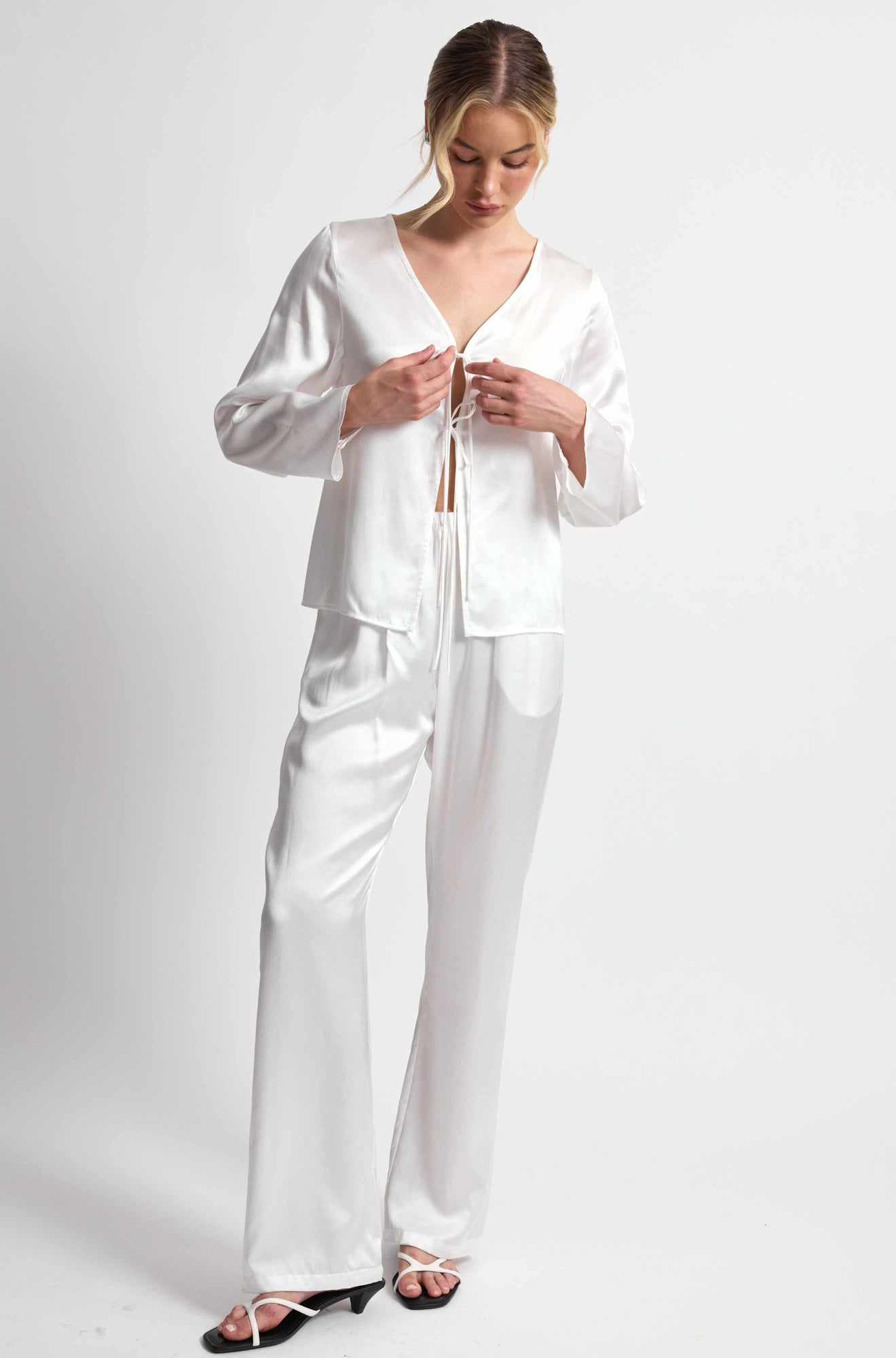 Woman wearing a white satin pajama set on a plain background