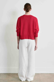 Person wearing a red sweater and white pants standing against a plain background