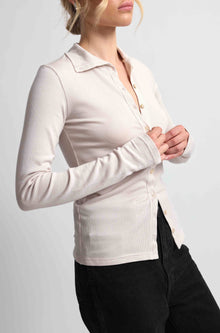 Woman wearing a pink button up top with black bottoms on a light grey background