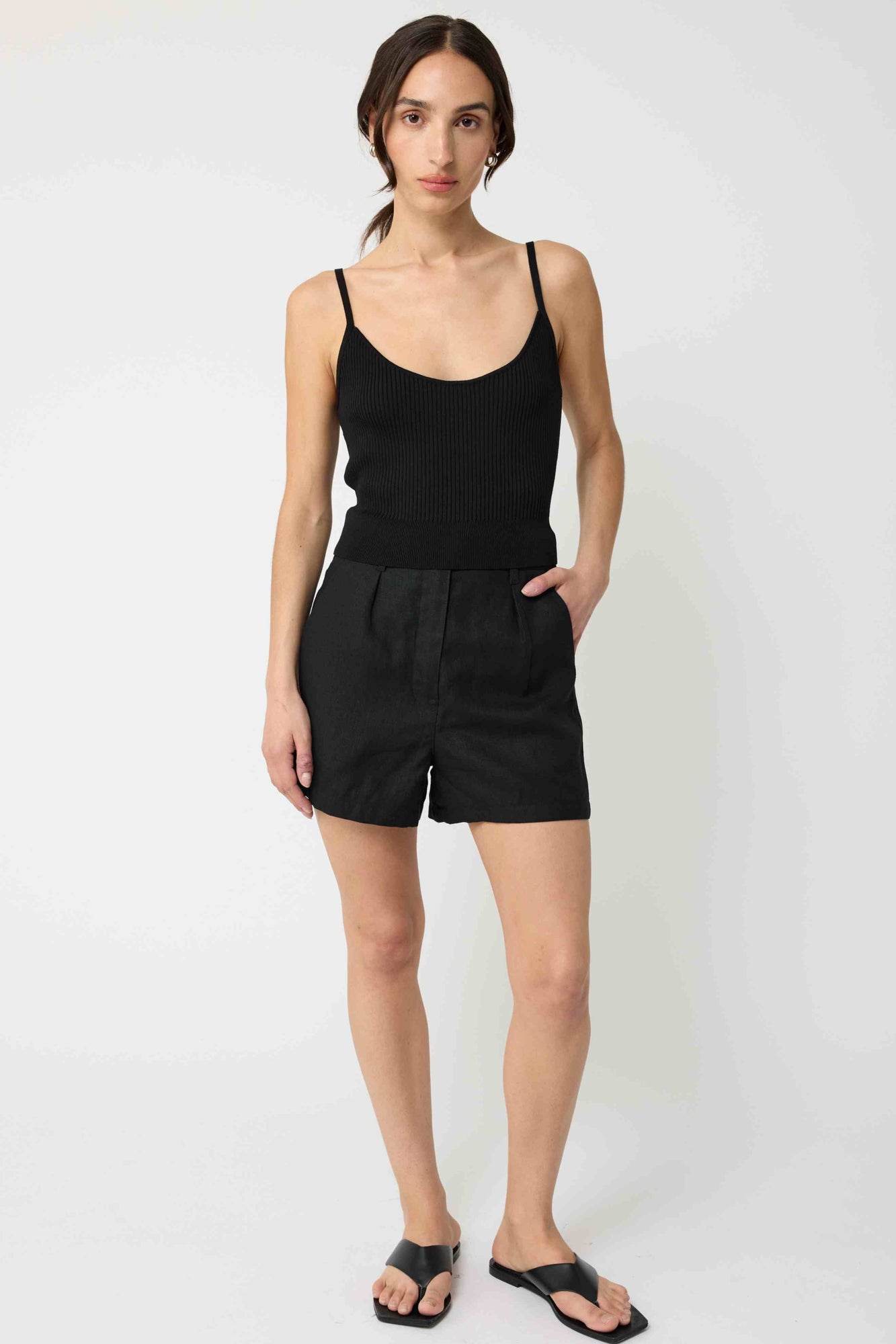 Woman wearing a black tank top and black linen shorts against a light grey background
