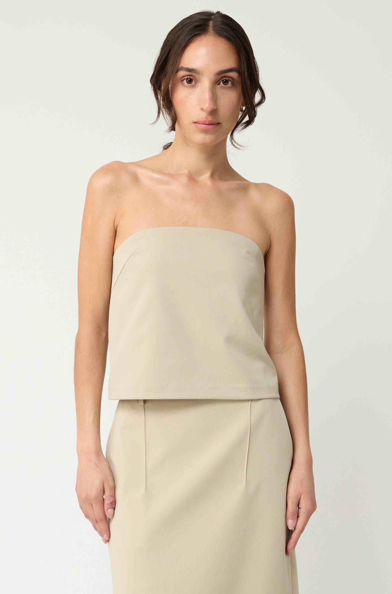 Woman wearing a beige strapless top with a matching beige skirt on a light grey background
