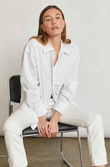 Woman wearing a white outfit sitting on a chair against a plain background