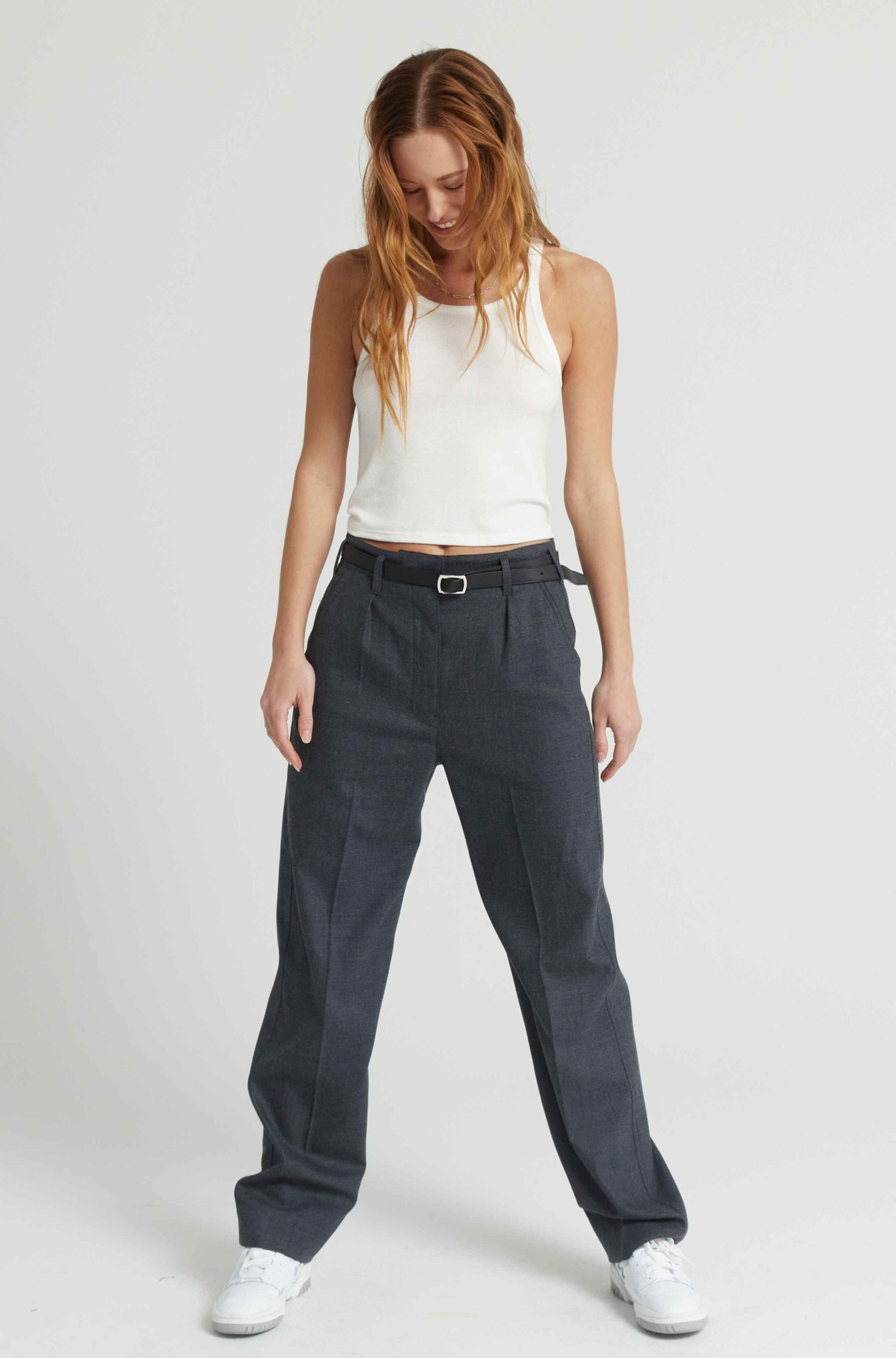 Woman wearing a white sleeveless top and dark pants on a plain background