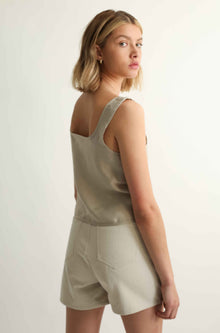 Woman wearing a beige sleeveless top and shorts on a light background