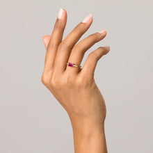 Model Close-up of a raised hand wearing a gold ring with a pink baguette gemstone against a light grey background