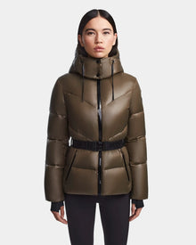 A woman wears the Rudsak CHRISTELLE S - L123524 Light Olive chevron quilted down puffer with hood, black zippers, and belted waist, standing facing forward against a plain light background.