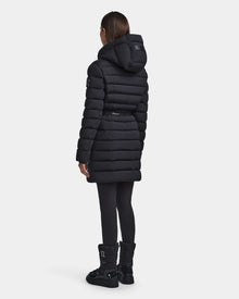 A person stands facing away from the camera against a plain light background, wearing the Rudsak FRIDA M - L123514 Black women's mid-length down jacket with removable hood, paired with black leggings and black boots.