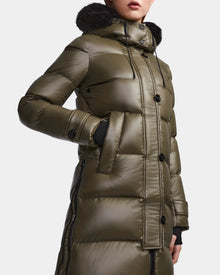 A person wears the Rudsak MEYA S - L123521 Light Olive women's down puffer coat with black buttons, a hood with dark fur trim, and hands in side pockets. The shiny olive green coat image is cropped at the nose and mid-thigh.