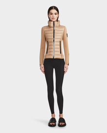 A woman faces forward against a white background, wearing the RUDSAK MABS - 8122020 TOFFEE lightweight beige activewear jacket, paired with black leggings and black slide sandals.