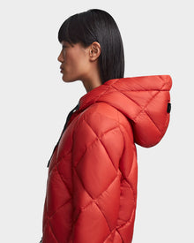 A woman with straight, dark hair and bangs is shown in profile wearing the Rudsak BALA - 8123614 Orange sustainable puffer jacket against a plain light gray background.