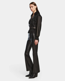 A woman stands in a three-quarter pose wearing the Rudsak HALA - 8124521 Black belted jacket with black leather flared pants and heeled boots, perfect as a chic fall look, against a plain white background.