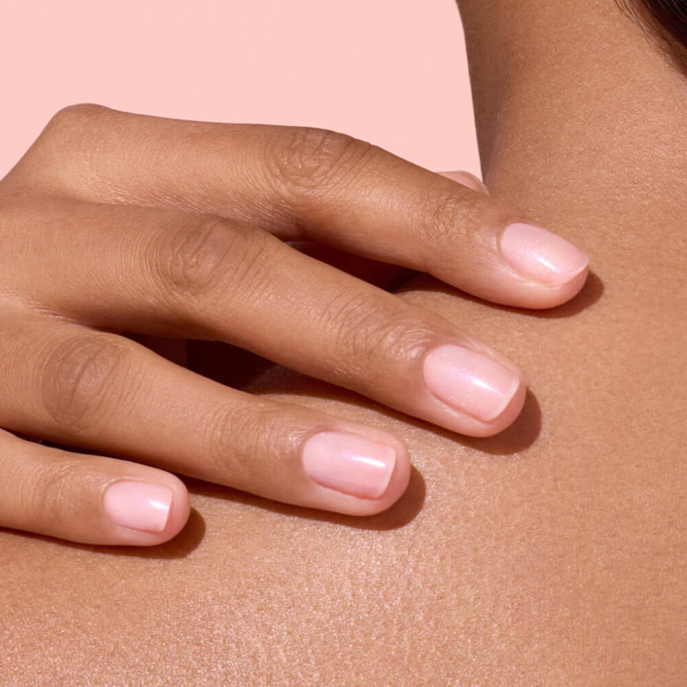 A close-up of a hand with neatly manicured nails painted light pink, gently resting on a persons shoulder against a soft pink background.