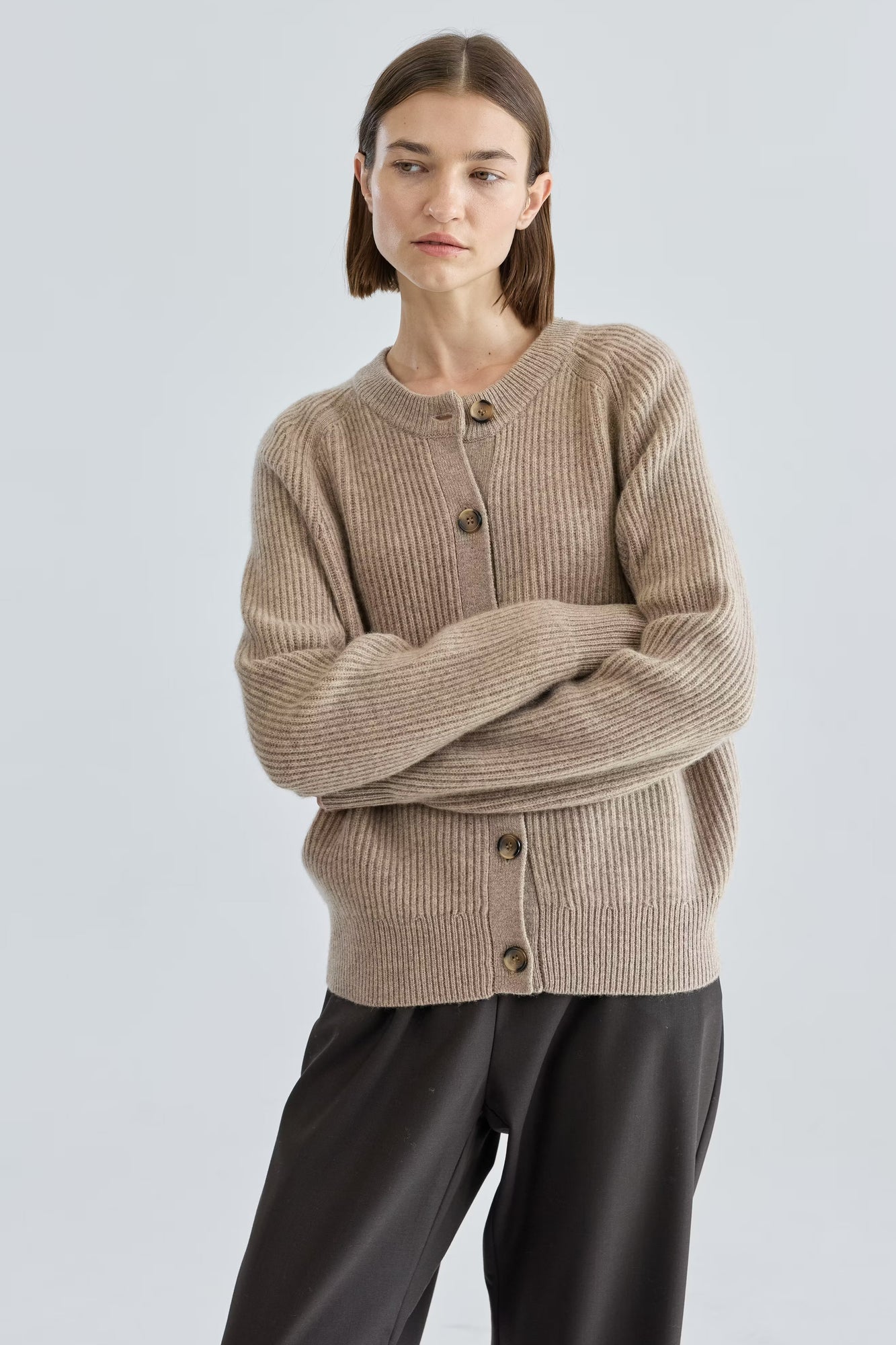 Woman wearing a beige cardigan with black buttons on a light gray background