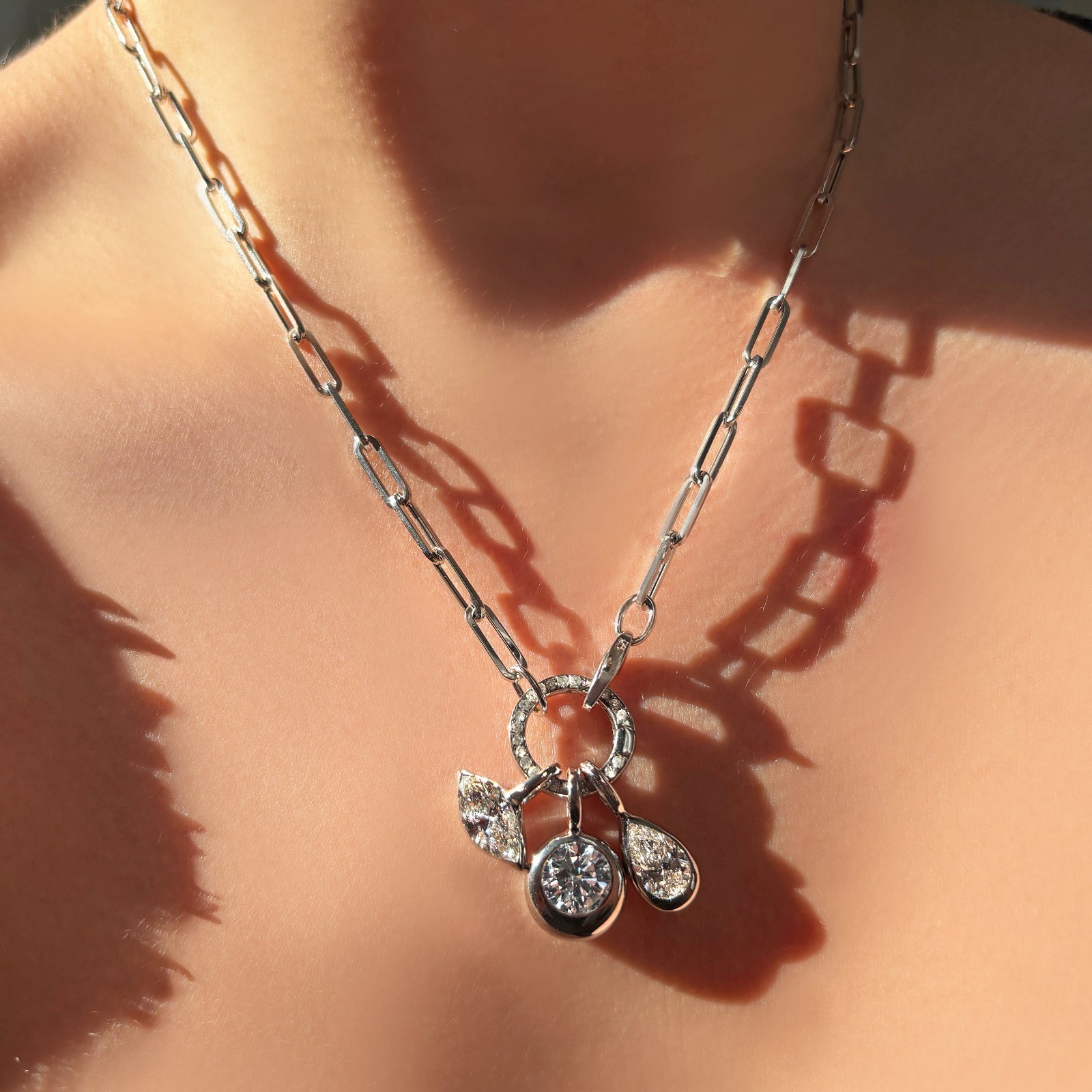 Molten solitaire charms hanging from a round pavé face charm lock on a chunky paperclip chain necklace - all sparkling in white gold. 