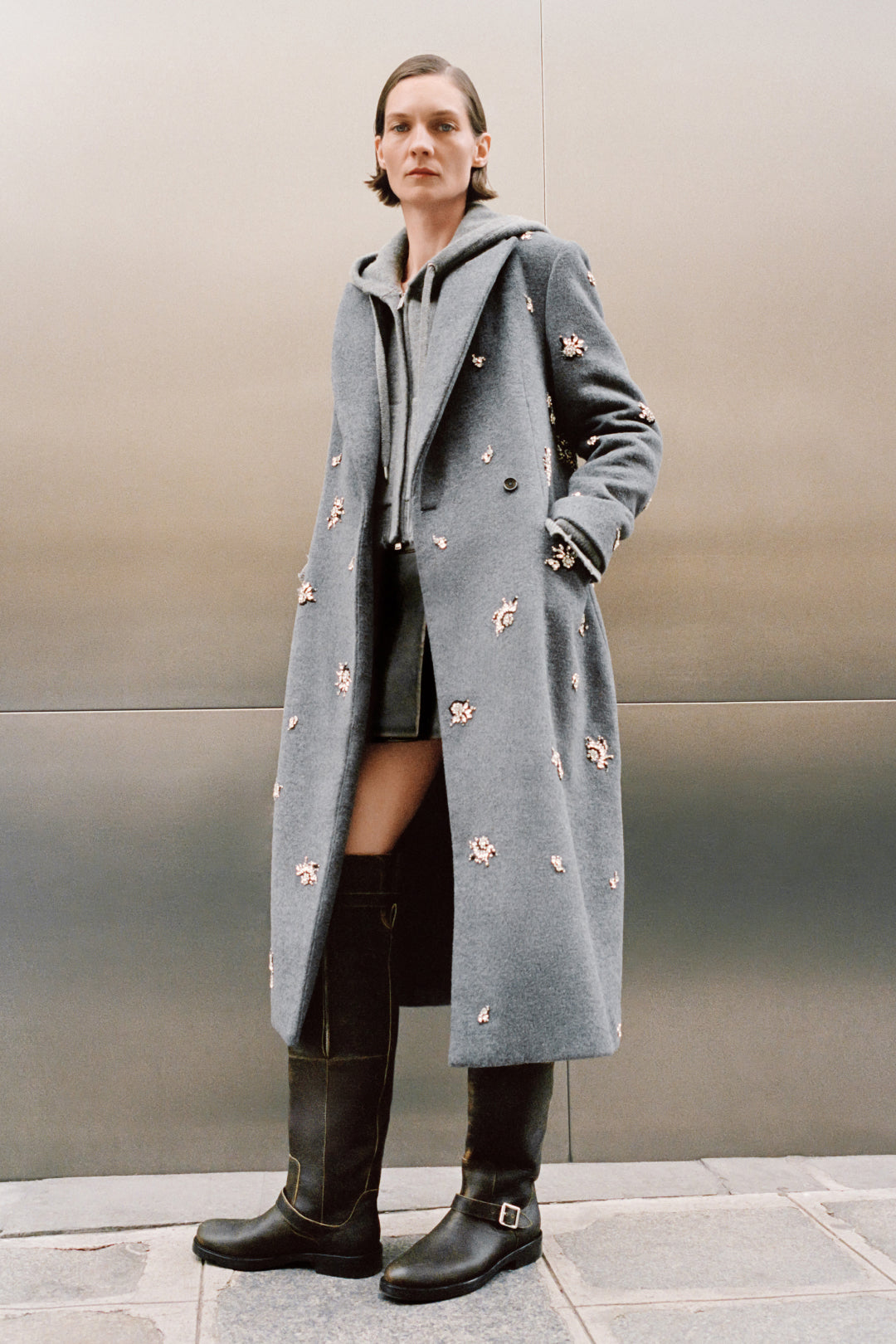 Black leather over-the-knee boot with buckle detail, worn with gray embellished coat.