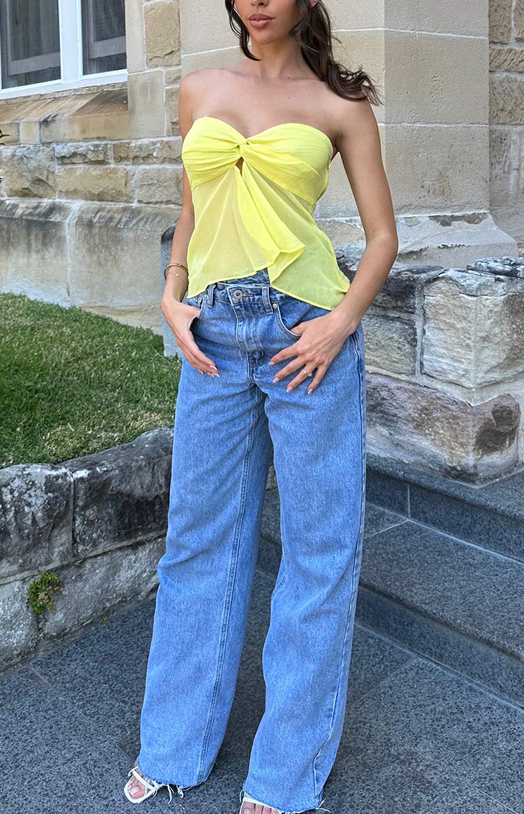 Yellow strapless top with a knotted bust detail, sheer fabric, and an asymmetrical draped hem
