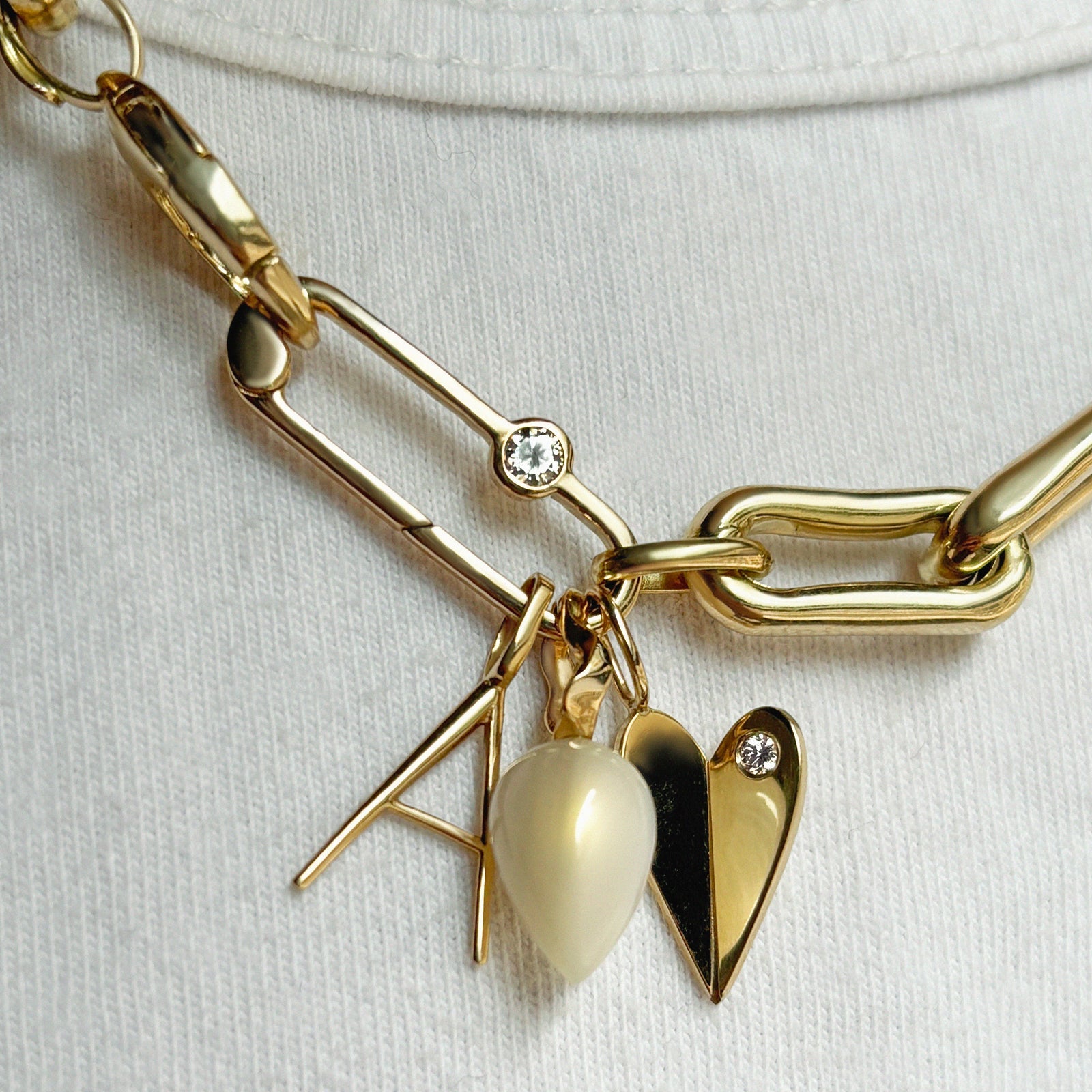 14K Gold Folded Heart Charm with white diamond styled on neck with multiple charms, hanging from chain and lock