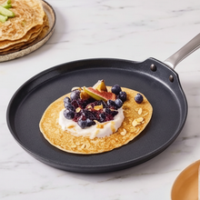 Golden pancake topped with blueberries, figs, and cream in a nonstick skillet